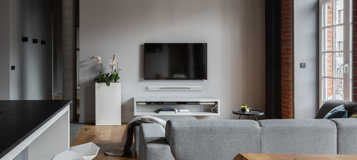 Sonos Arc wall mount in stunning smart home entertainment setting with wall mounted Tv and light-filled living room furniture setting. 